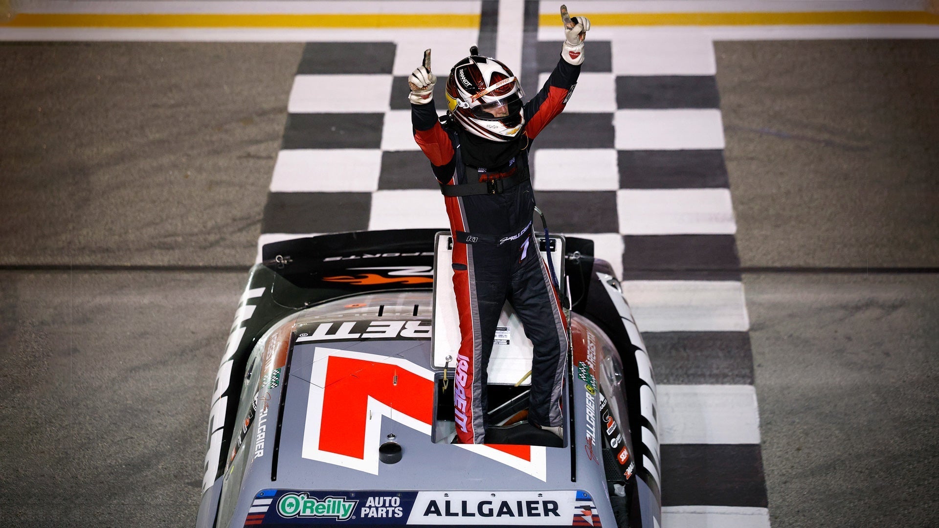 Justin Allgaier stands on his car in a custom K1 RaceGear suit after winning Focused Health 250.